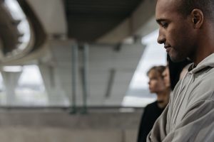 Profile of a pensive man under a modern bridge with blurred people in the background.